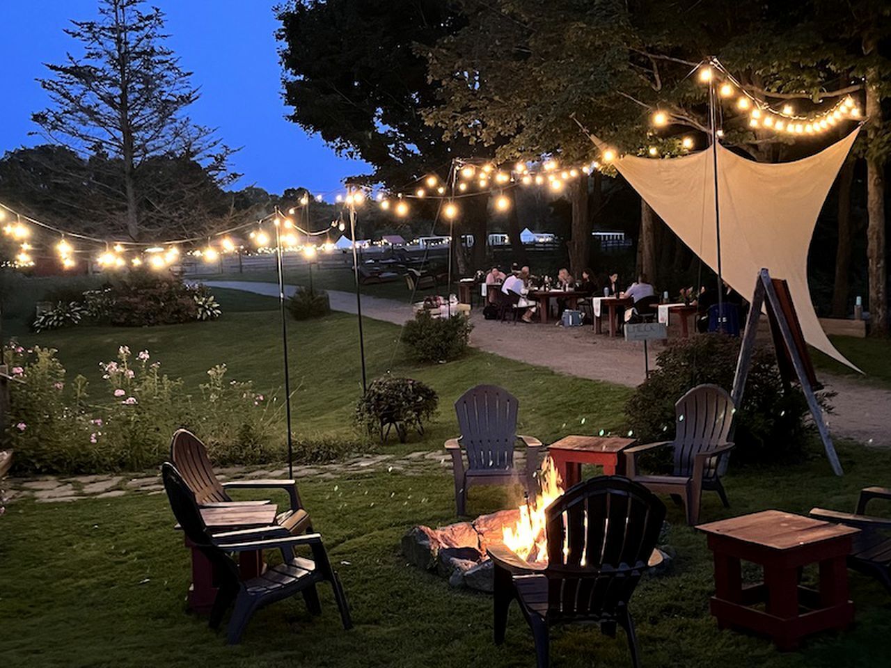 Un espace extérieur aménagé avec des chaises, des tables, un foyer et des guirlandes lumineuses.