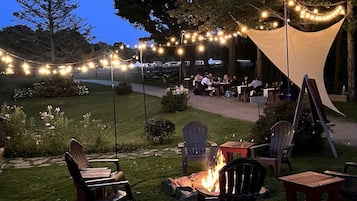 Un espace extérieur aménagé avec des chaises, des tables, un foyer et des guirlandes lumineuses.