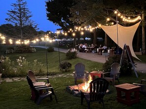 An outdoor seating area with chairs, tables, a fire pit, and string lights.