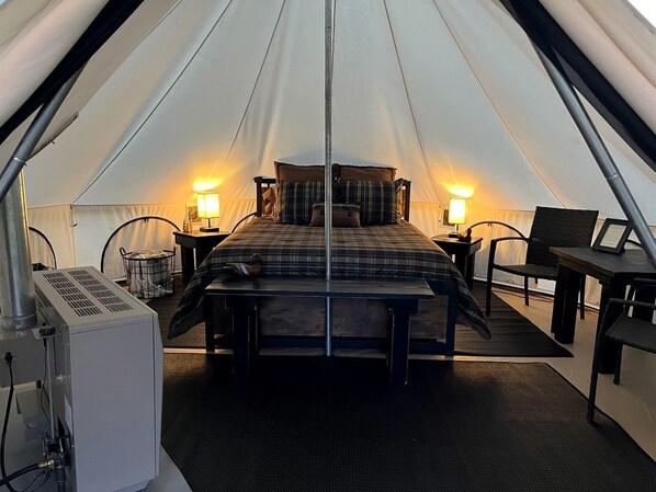 A tent with a bed, two bedside tables, a chair, and a table.