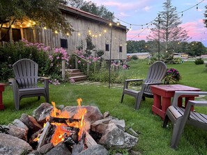 A rustic outdoor setting with a fire pit, wooden chairs, and a red table.