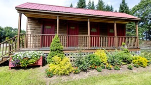 A log cabin with a red roof, wooden porch, and a garden with various plants and flowers. - Adult Only Bell Tent Perfect for a Romantic Getaway in Turner, Maine (Turner)