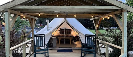 A wooden gazebo with a tent interior, two chairs, and a bench.