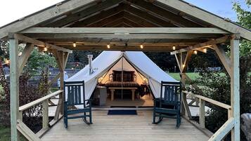 Un kiosque en bois doté d’une structure intérieure en forme de tente, de deux chaises et d’un banc.