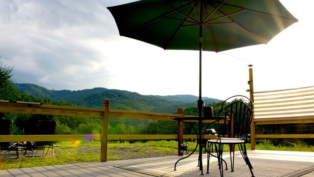 A deck with a table and chairs, an umbrella, and a view of a mountain range. - Roan Mountain Glamping Yurt, Ideal to Hike the Appalachian Trail (Roan Mountain)