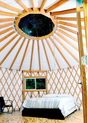 A yurt with a circular skylight, a bed, a window, and a lattice wall. - Roan Mountain Glamping Yurt, Ideal to Hike the Appalachian Trail (Roan Mountain)