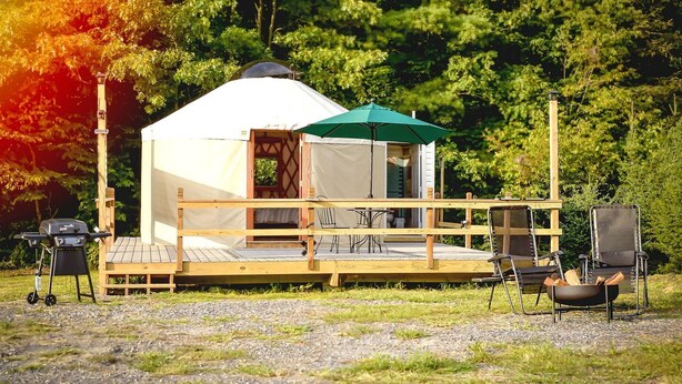Een tent met een houten terras, een tafel, stoelen en een barbecue.