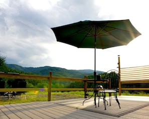 Eine Terrasse mit Tisch, Stühlen und Sonnenschirm, mit Blick auf ein Gebirge.