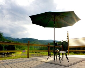 A deck with a table and chairs, an umbrella, and a view of a mountain range. - Roan Mountain Glamping Yurt, Ideal to Hike the Appalachian Trail (Roan Mountain)