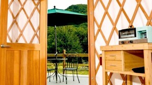Een houten interieur met een tafel en stoelen buiten, een houten bureau met laden en een groene parasol.