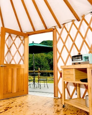 A wooden interior with a table and chairs outside, a wooden desk with drawers, and a green umbrella.