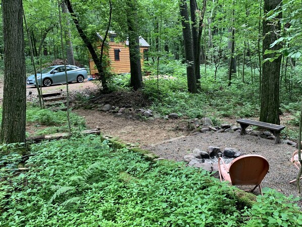 Zona boscosa con una cabaña, un coche y un banco.