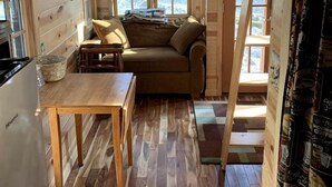 A cozy cabin interior with a loft bed, a sofa, a dining table, and a kitchen area. - Many Pines Tiny House in in Chetek, WI (Chetek)