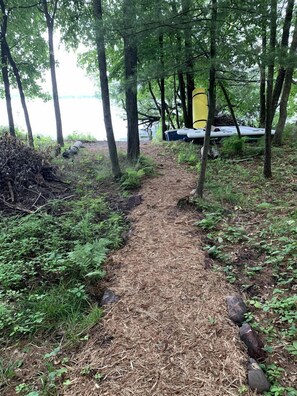 A forested area with a narrow path leading to a yellow tent and a white vehicle.