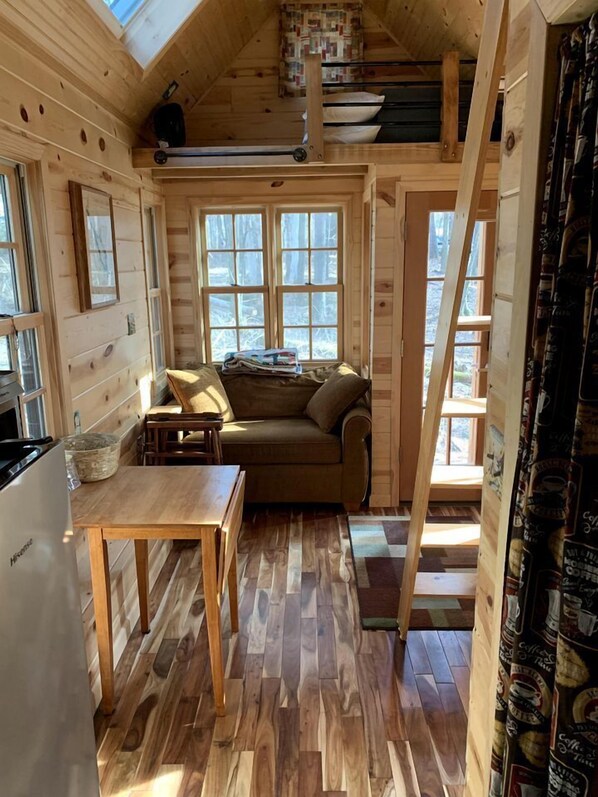 A cozy cabin interior with a loft bed, a sofa, a dining table, and a kitchen area. - Many Pines Tiny House in in Chetek, WI (Chetek)