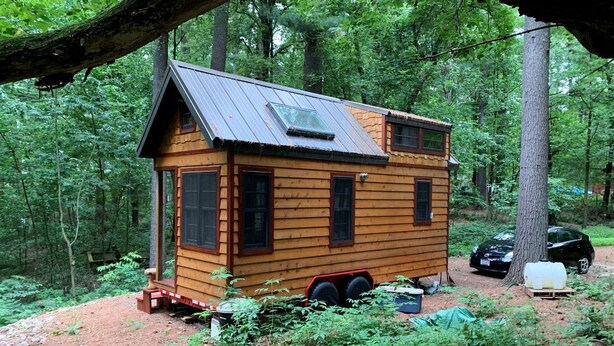 A small wooden cabin with a metal roof, surrounded by dense forest.