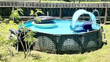 An above-ground swimming pool with a cover, surrounded by a wooden fence and grass.