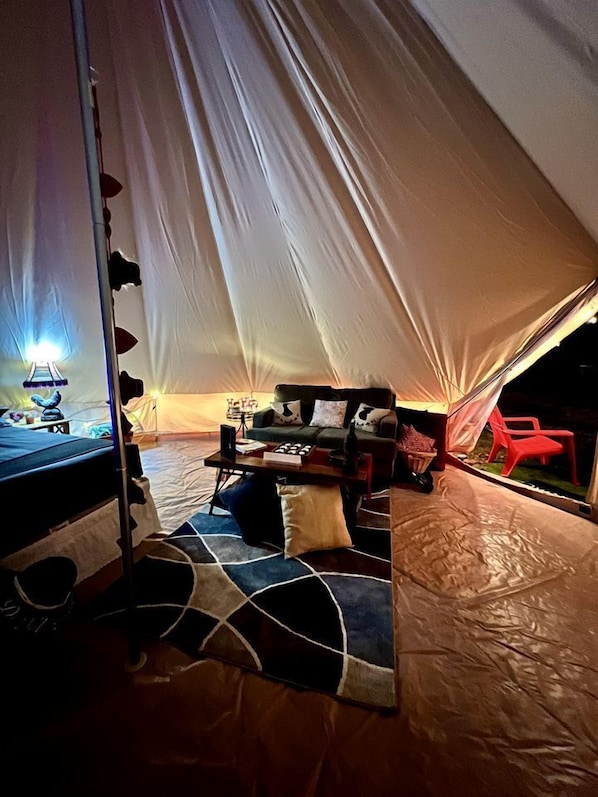 A tent interior with a bed, a sofa, a table, and a chair.