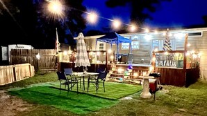 Patio esterno ben illuminato con tavolo e sedie, zona relax coperta e barbecue.