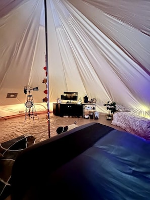 A tent with a bed, a small table, a clock, and a plant.