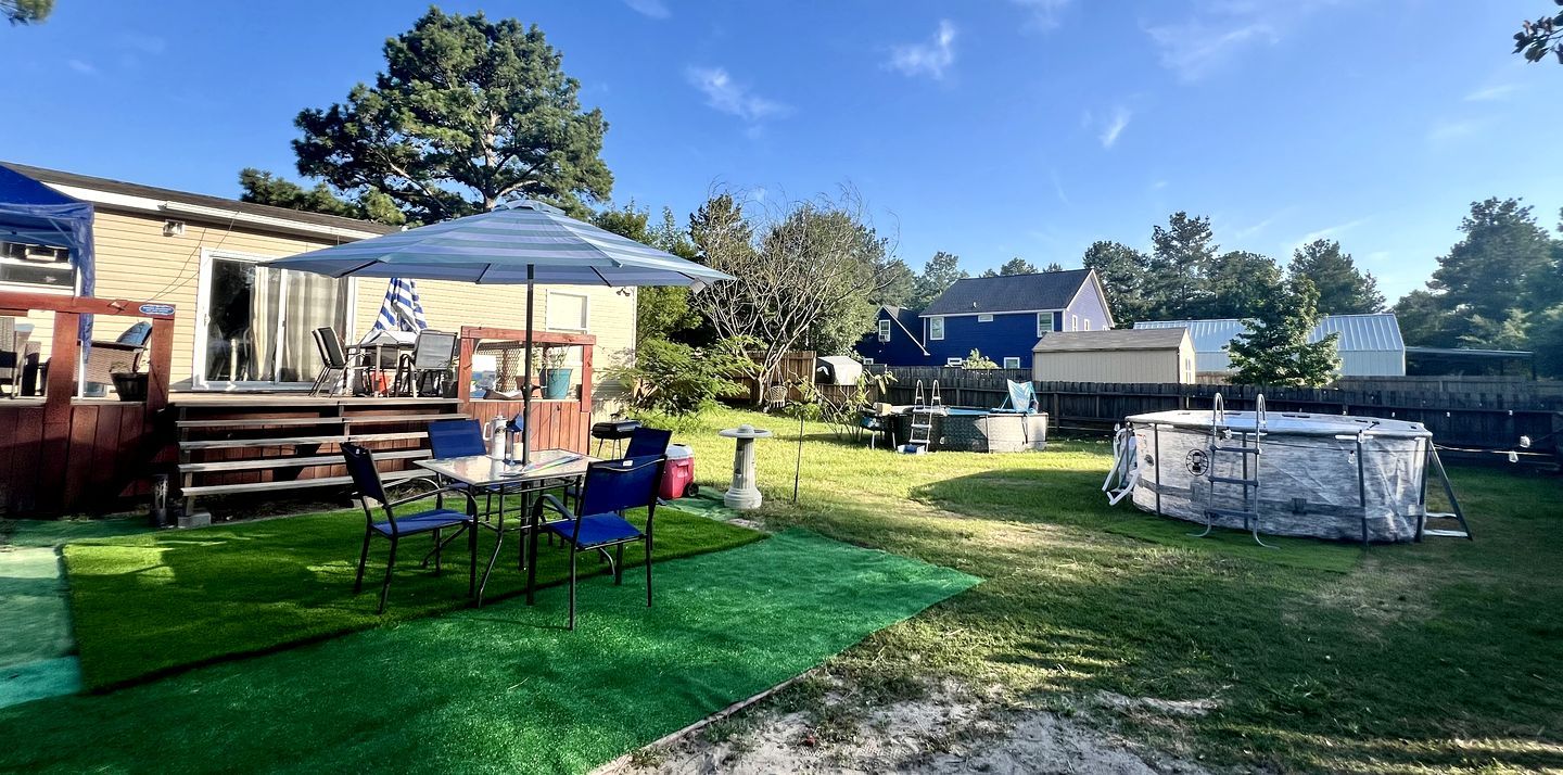 Een achtertuin met een overdekte patio, een tafel met stoelen, een jacuzzi en een zwembad.