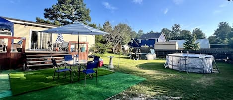 A backyard with a covered patio, a table with chairs, a hot tub, and a swimming pool.