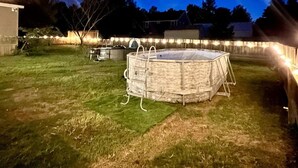 Un giardino sul retro con piscina coperta, barbecue e luci a catena.