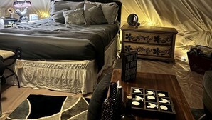 Un alloggio in tenda con un letto, un comodino, una lampada e oggetti decorativi.