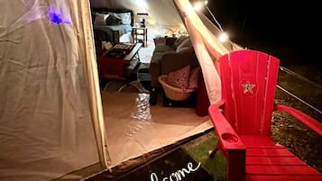 A tent interior with a red chair, a welcome mat, and a table with a lamp.