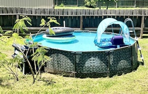 An above-ground swimming pool with a cover, surrounded by a wooden fence and grass.