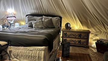 A tented accommodation with a bed, bedside table, lamp, and decorative items.