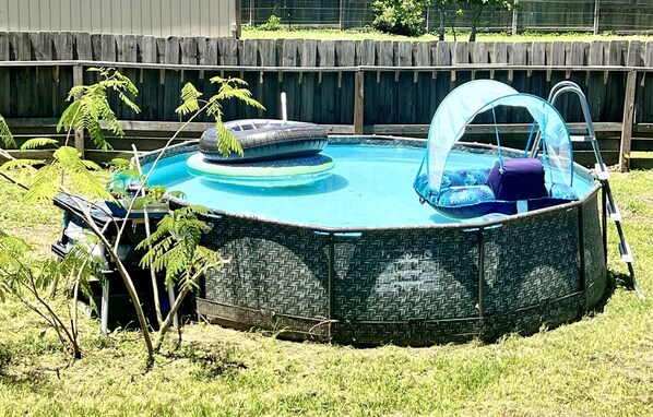 An above-ground swimming pool with a cover, surrounded by a wooden fence and grass.