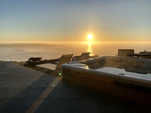 A hot tub with a sunset view, lounge chairs, and a stone deck.