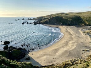 A coastal landscape with a sandy beach, rocky outcrops, and grassy hills.