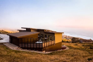 A modern house with a flat roof, large windows, and a view of the ocean.