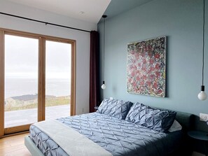 Un dormitorio con una cama grande, vista al océano y un cuadro abstracto moderno en la pared.