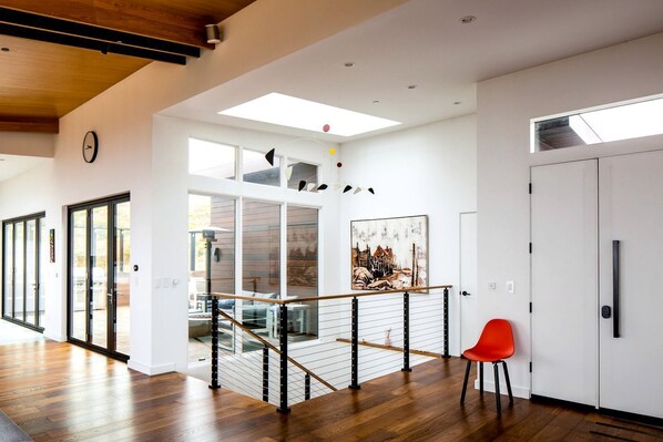 A modern interior with a wooden floor, a staircase with glass railings, a red chair, and a painting on the wall.