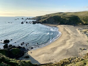 Et kystlandskab med sandstrand, klippeformationer og grønne bakker.