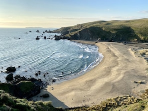 A coastal landscape with a sandy beach, rocky outcrops, and grassy hills.
