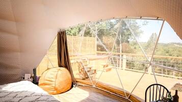 A tented room with a bed, a pillow, a table with a bottle, and a chair.