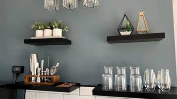 A kitchen with a black countertop, white cabinets, and a grey wall. There are three hanging light fixtures, a plant, and a decorative item on the wall.