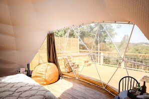 Una habitación con tienda de campaña, una cama, un almohadón, una mesa con una botella y una silla.