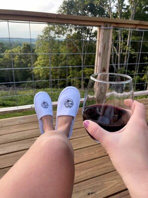 A person sitting on a wooden deck with a railing, holding a glass of red wine.