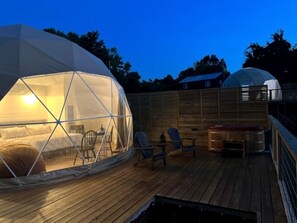 A geodesic dome structure with a bed, chairs, and a table on a wooden deck.