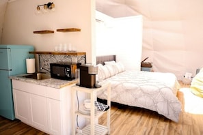 A compact room with a kitchenette, a bed with a canopy, and a small table with a lamp.