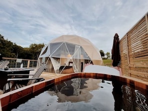 A dome-shaped structure with a pool in front, wooden deck, and a fence.