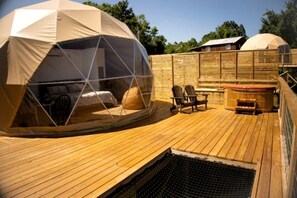 A dome-shaped tent with a bed inside, a wooden deck, and a hot tub. - Vintage Themed Geodome with a Cedar Hot Tub and Mountain Views, Perfect for a Romantic Getaway in Eureka Springs (Eureka Springs)