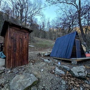En enkel, rustik träbod och en blå metallkonstruktion i ett skogsområde.
