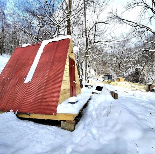 Ein mit Schnee bedecktes Holzgebäude mit rotem Dach, umgeben von schneebedeckten Bäumen.