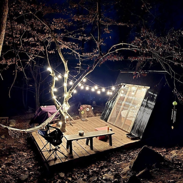 A wooden deck with a table and chairs, string lights, and a small waterfall feature.